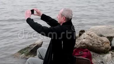 坐在<strong>湖岸</strong>上的中年老人。 孤独成熟的男人在银行拍自拍照片。 概念